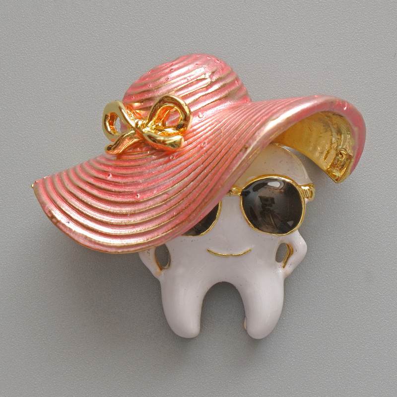 Brooch 'Tooth in a Hat' with enamel, white, pink, and black, golden metal 33x30mm